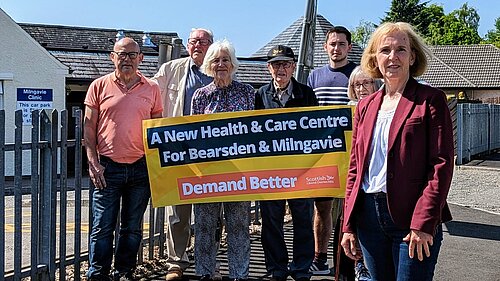 Susan Murray in front of campaigners holding up a banner calling for a new health and care centre for Milngavie and Bearsden