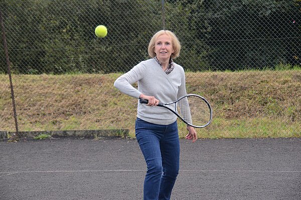 Susan Murray MP on a tennis court with a racket as she looks to hit a forehand shot as a tennis ball approaches.