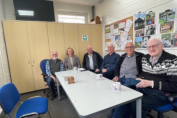 Susan Murray sitting at a table with a group from the men from the Milngavie and Bearsden Men's Shed.