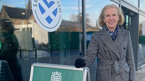 Susan Murray standing next to a sign advertising an advice surgery as MP for Mid Dunbartonshire.