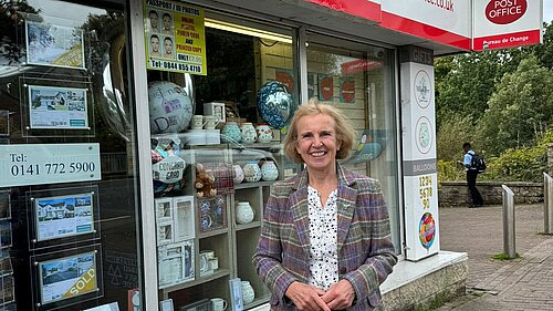 Susan Murray, MP for Mid Dunbartonshire, standing smiling in front of a post office.